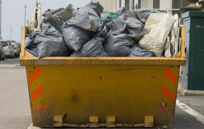 bags of garbage stacked high within a yellow roll away container